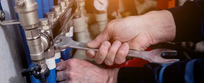 hands holding wrench on water pipes, plumbing problems that can arise in hot weather