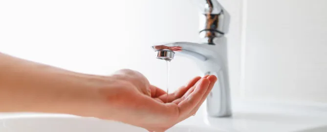 A frustrated homeowner testing low water pressure at a kitchen sink faucet.
