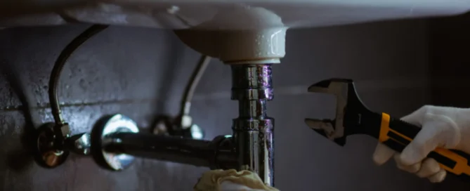 Person working under a sink wearing white gloves, holding a wrench to the pip.