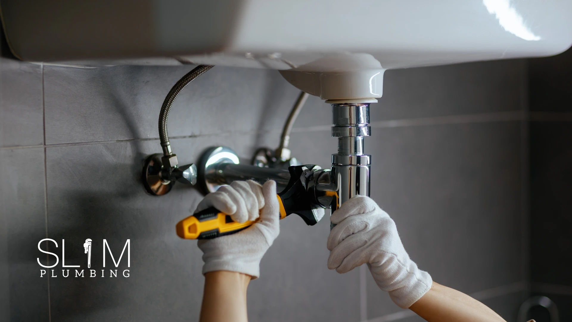 Prevent Clogged Drains Before They Start - Slim Plumbing plumber tightening under-sink drain pipe with wrench to keep drains clear